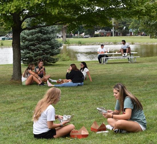 学生们坐在池塘边的草地上聊天